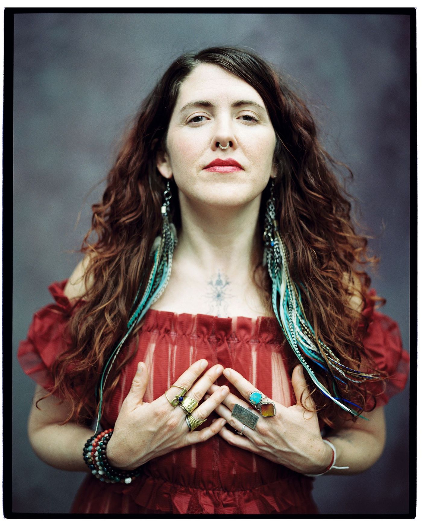Portrait of Carolee Beckham in a red dress, hands at her heart, turquoise feathers in her hair.