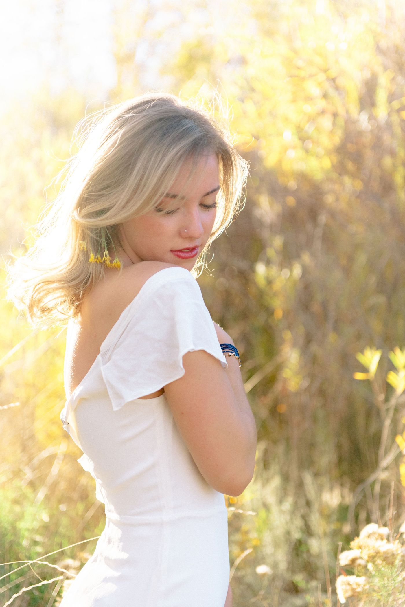 A young woman in a white dress glances down, her hair glowing in warm backlight.