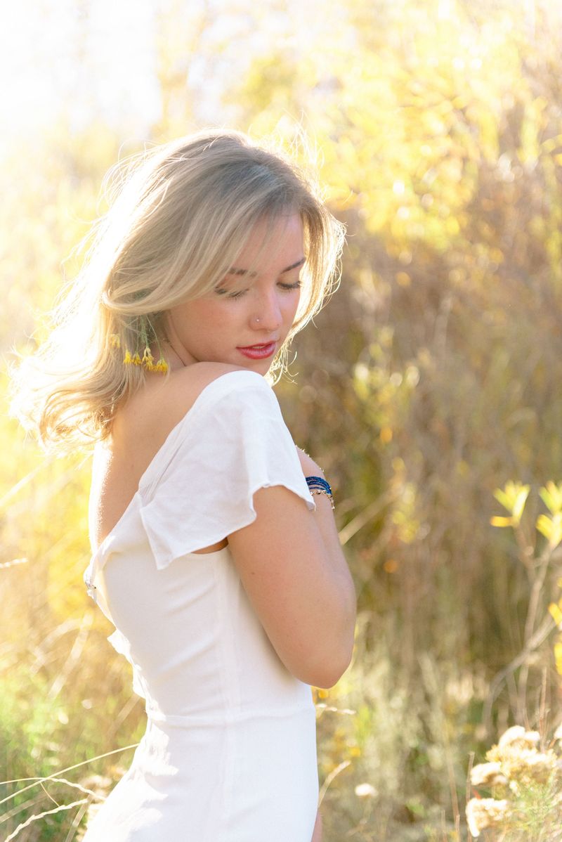 A young woman in a white dress glances down, her hair glowing in warm backlight.